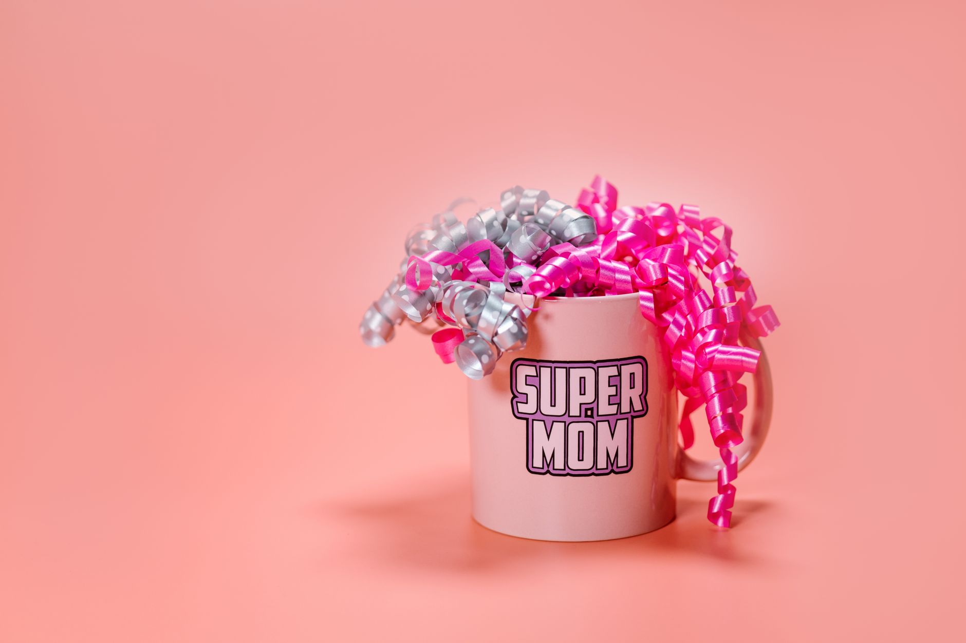 Różowy kubek z napisem "SUPER MOM" ozdobiony różowymi i srebrnymi wstążkami