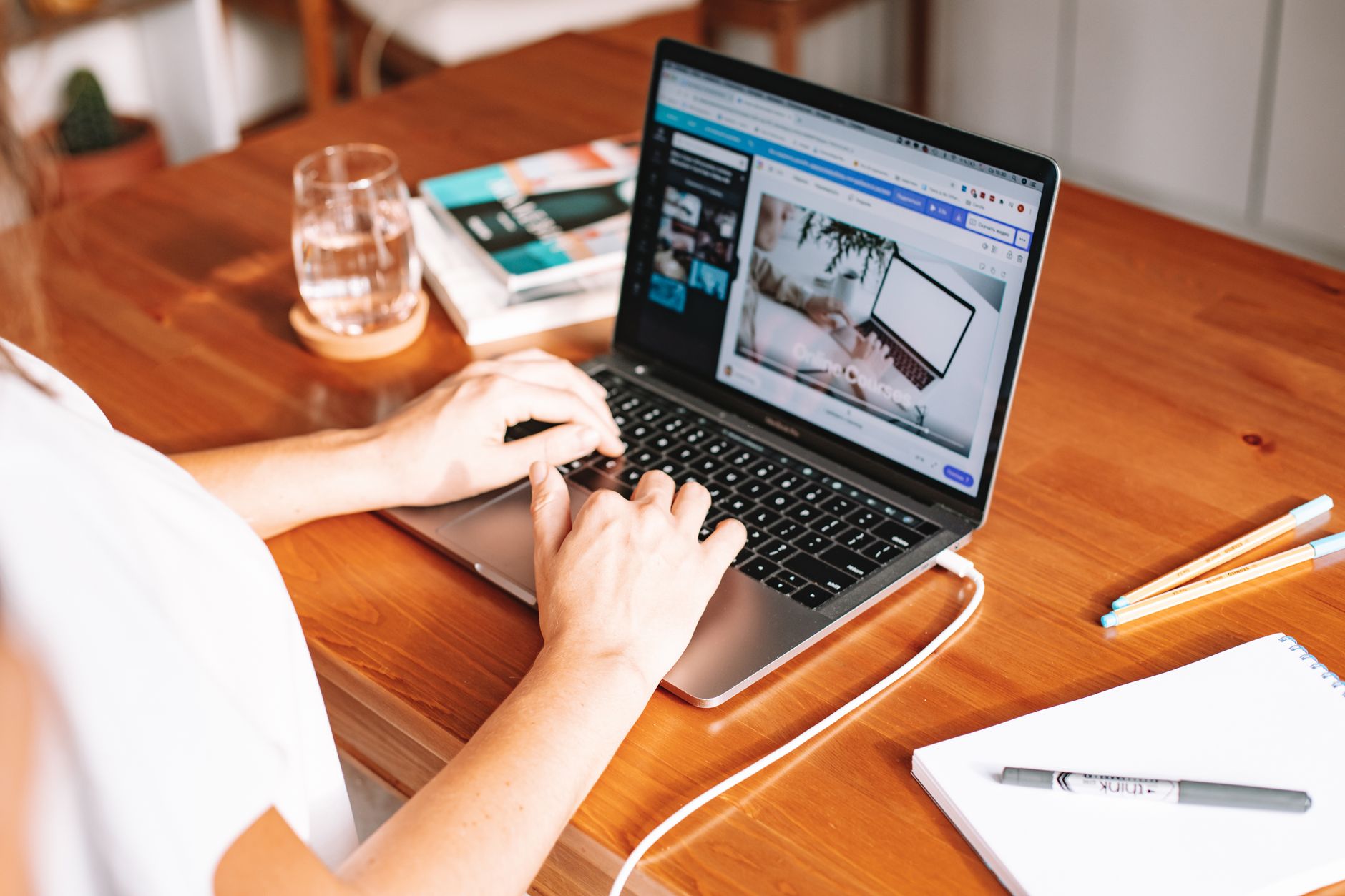 Ręce na klawiaturze laptopa wyświetlającego stronę internetową, biurko z akcesoriami