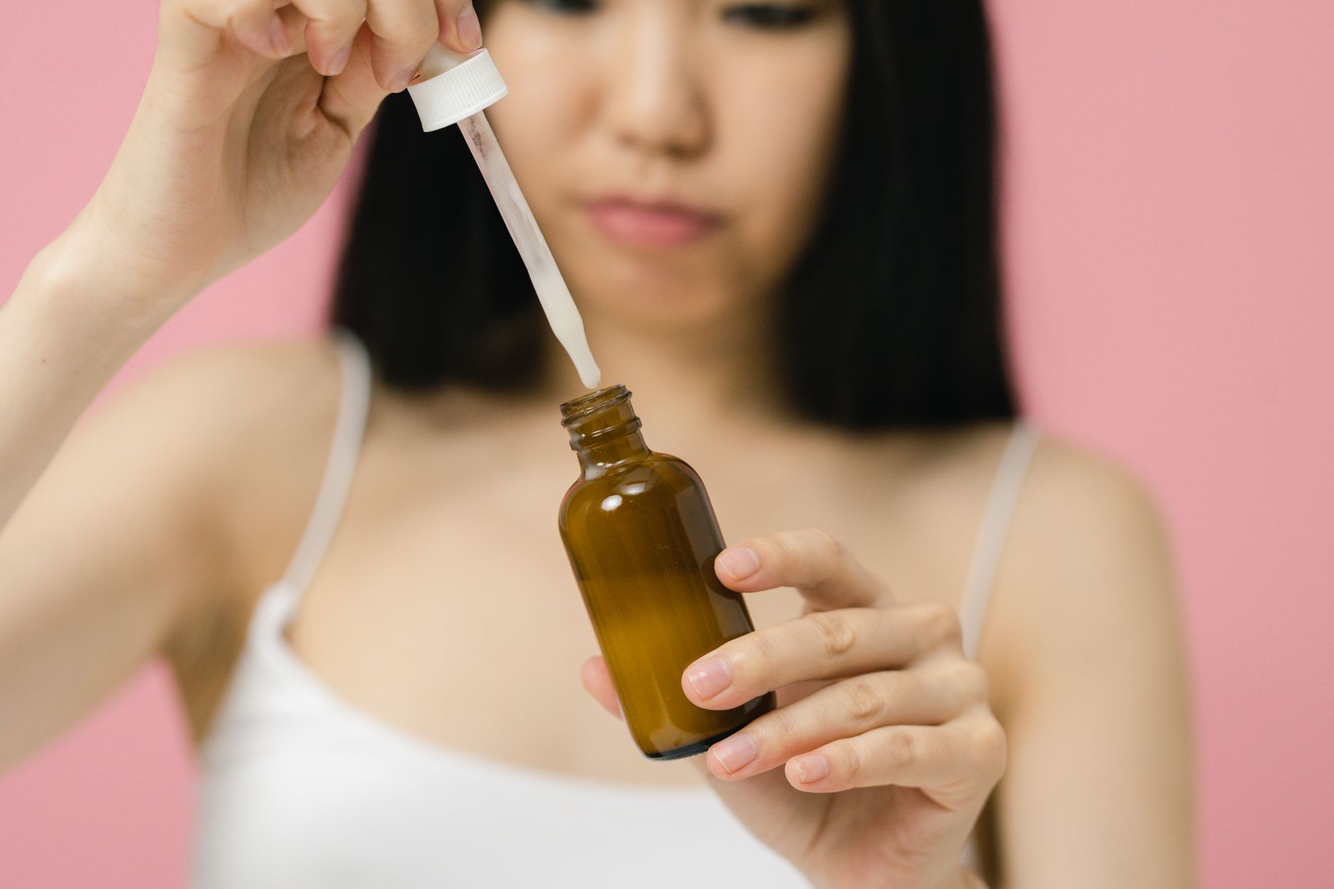 Kobieta trzymająca butelkę z pipetą zawierającą olejek na różowym tle