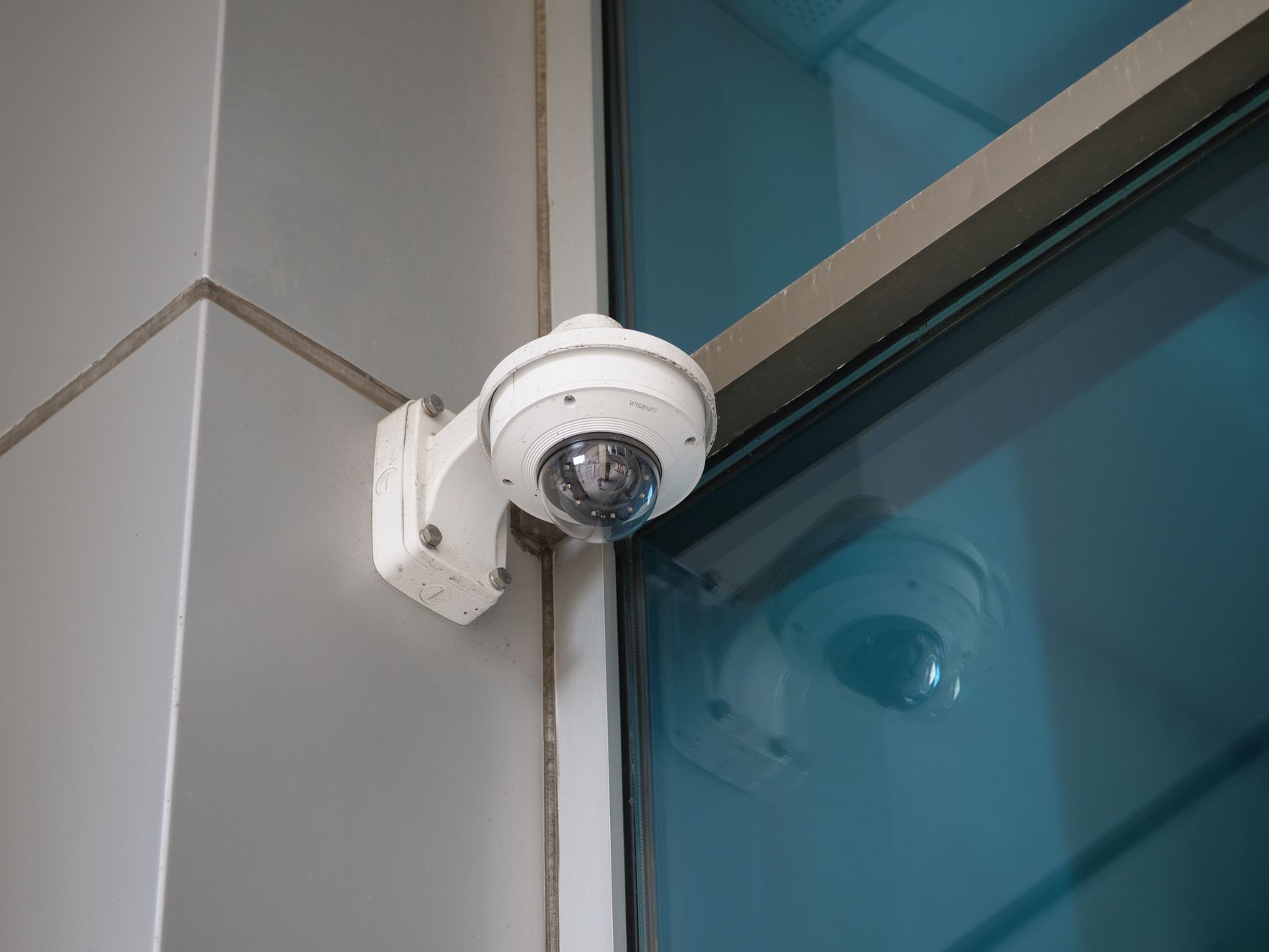 Kopułkowa kamera monitoringu z obiektywem kulistym na białym tubie przy wejściu