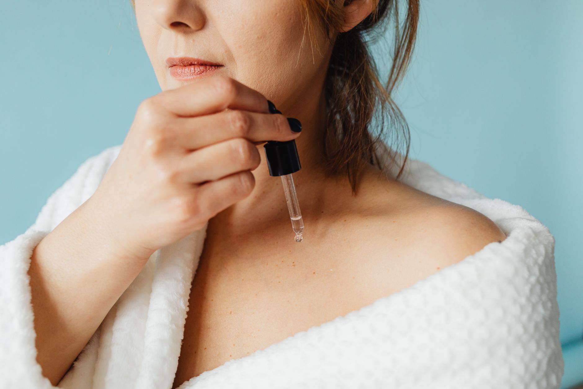 Kobieta nakrapla rozświetlający serum na szyję i dekolt, demonstrując aplikację produktu