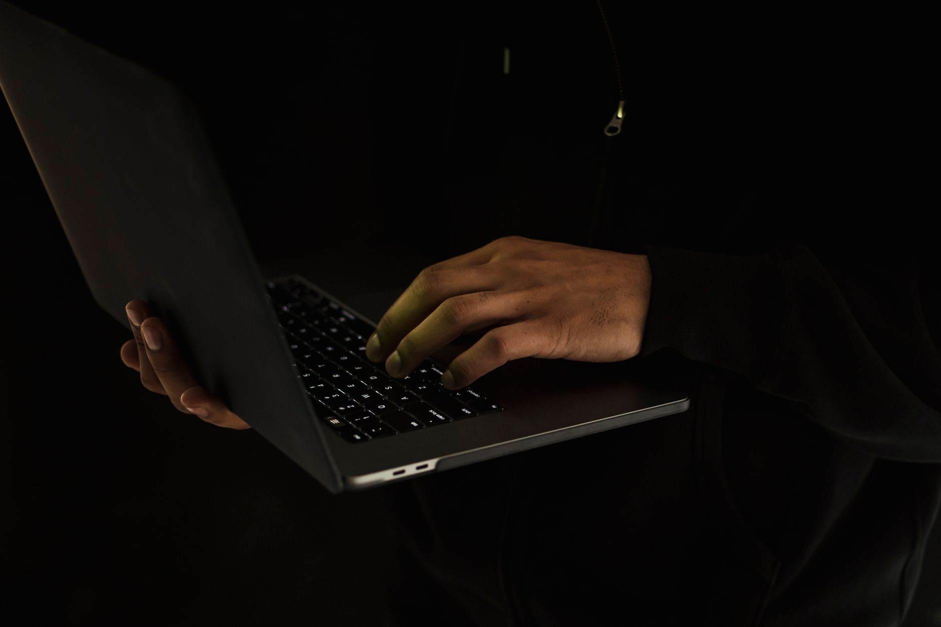 Ręce osoby piszącej na klawiaturze ciemnego laptopa na czarnym tle